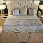 Pat matrimonial cu tăblie decorativă înaltă și bază capitonată (opțiune somieră rabatabilă / ladă), dulap generos cu uși lăcuite 3D și oglindă, 2 noptiere cu sertare și comodă toaletă cu oglindă.